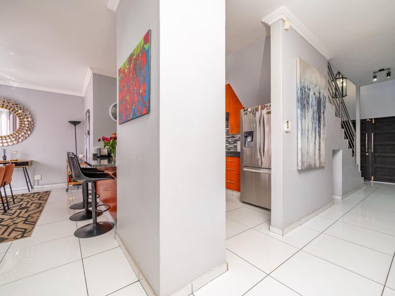 Open plan living area featuring tiled flooring, a breakfast bar, and a view into the kitchen, with a staircase leading to the upper level.