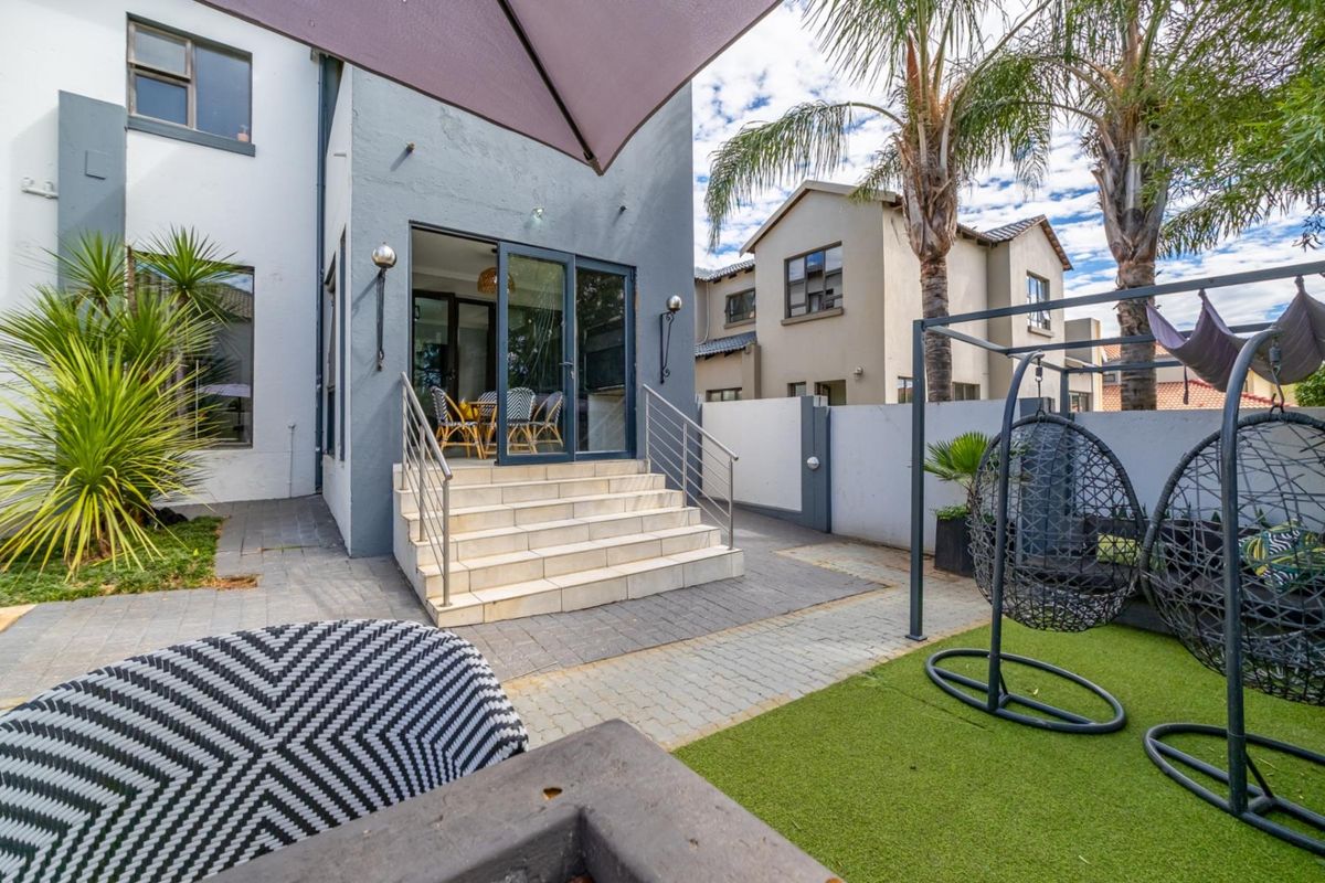 A well-maintained rear patio area featuring paved steps leading to glass sliding doors, complemented by a small artificial lawn and perimeter walling.