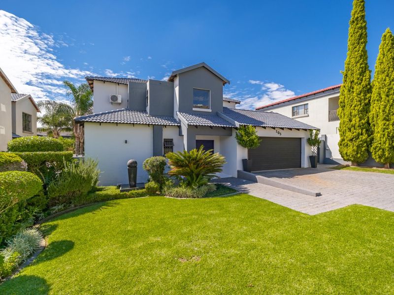 A well-maintained double-story residential house featuring a paved driveway, double garage, tiled roof, and a neatly landscaped front garden.