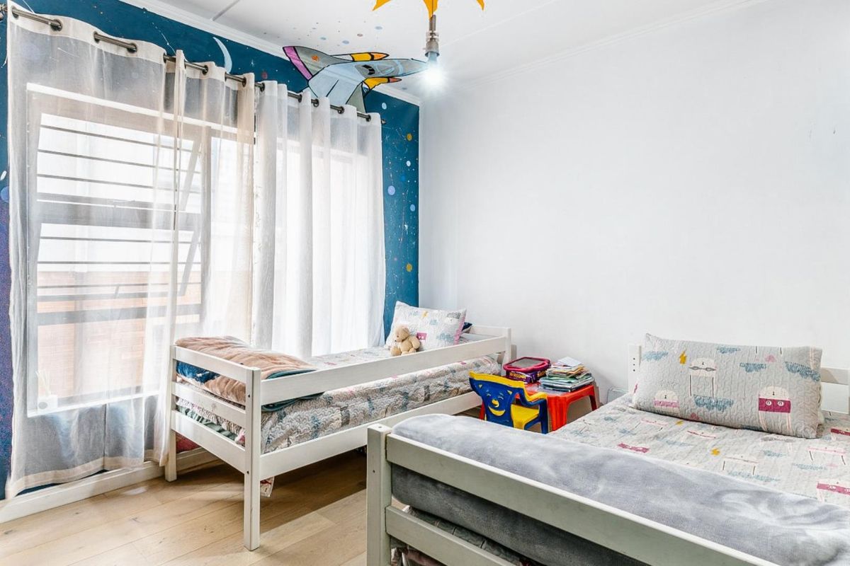 A bright bedroom featuring light wood-look flooring, a large window with sheer curtains, and a decorative space-themed accent wall.