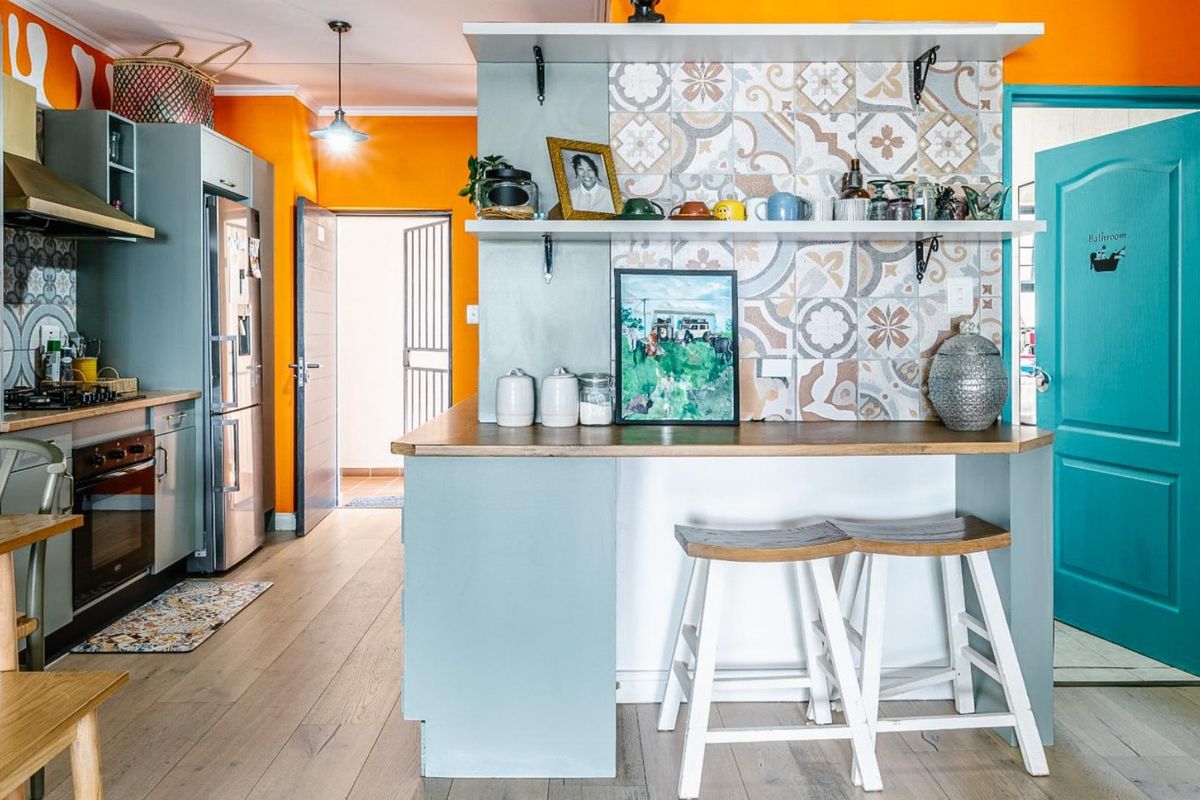 A vibrant kitchen featuring a breakfast bar with decorative tiled backsplash, built-in cabinetry, integrated oven, and hob, finished with light wood-look flooring.