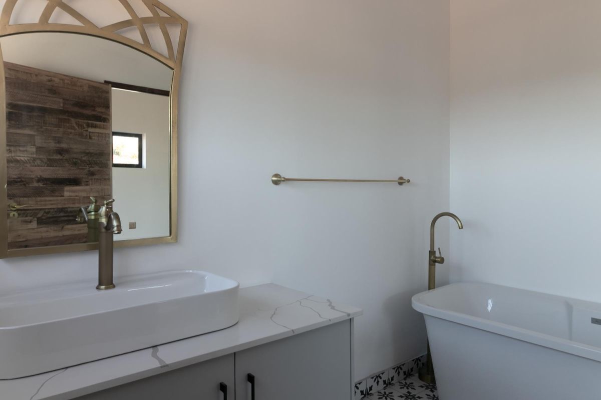 Modern bathroom featuring a sleek vanity with stone countertop, vessel sink, freestanding bathtub with brass fixtures, and decorative floor tiling.