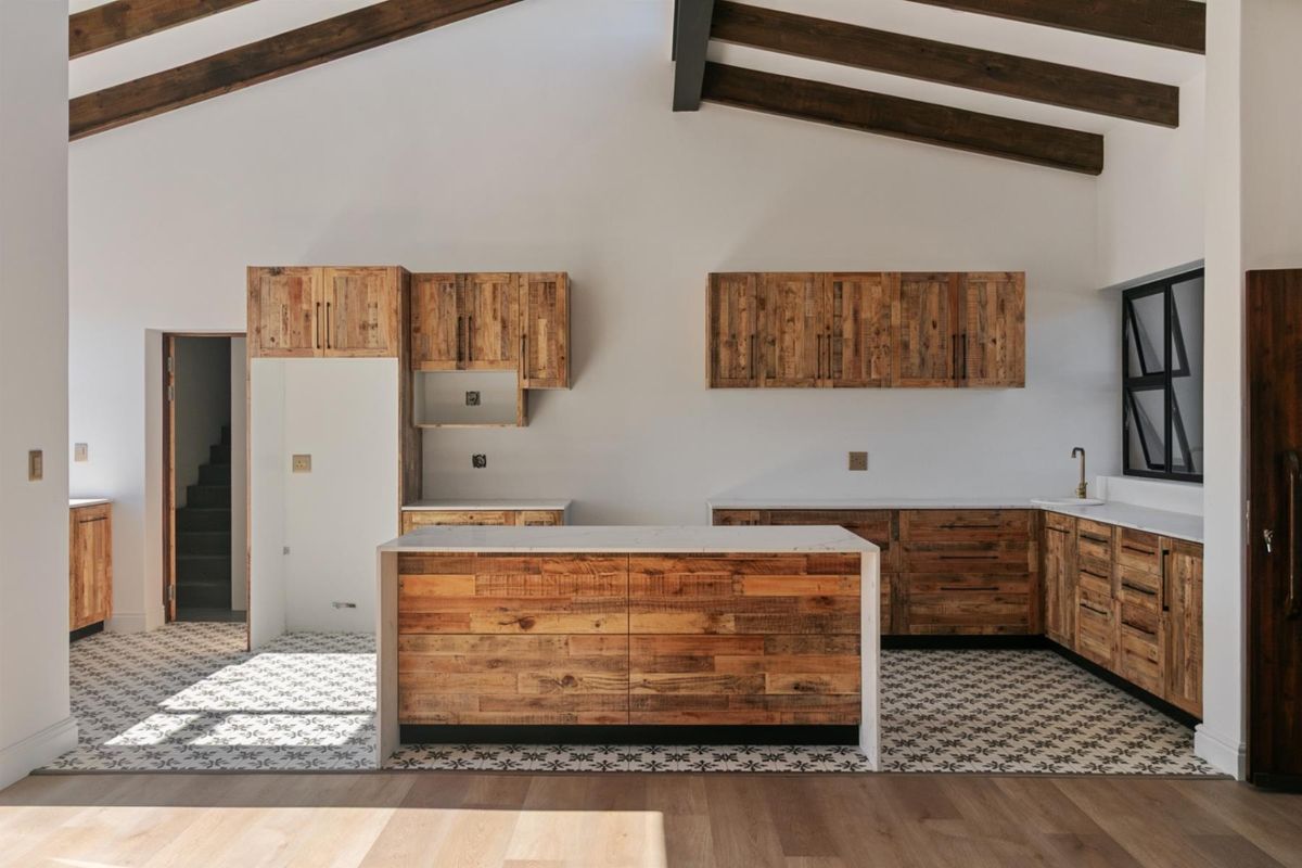 Modern kitchen featuring rustic timber cabinetry, a central island with stone countertop, patterned floor tiles, and exposed timber ceiling beams.