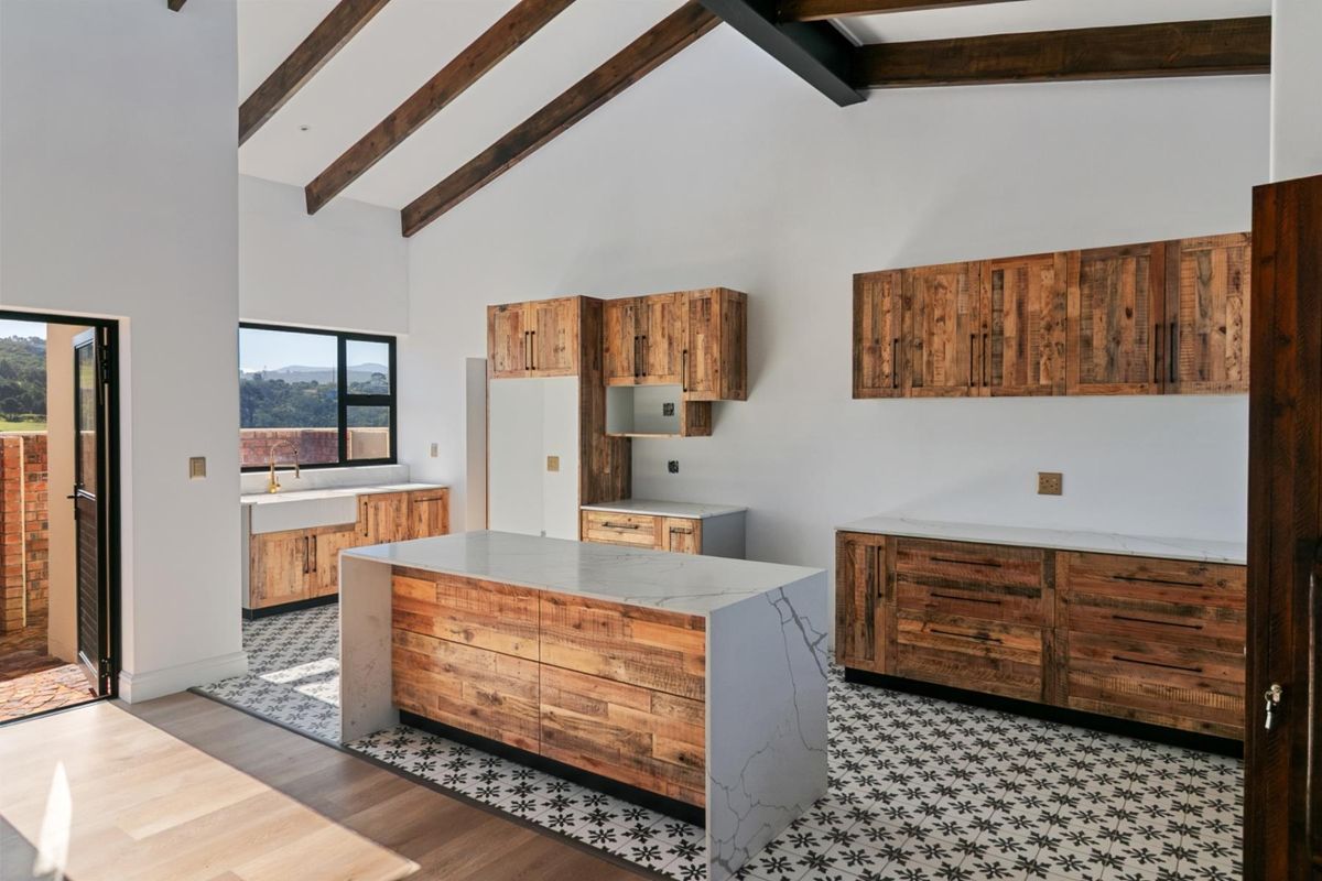 Modern kitchen featuring rustic timber cabinetry, a waterfall-edge stone island, farmhouse sink, and vaulted ceilings with exposed timber beams.