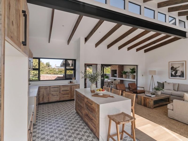 Spacious open-plan living area featuring a modern kitchen with quartz island, exposed timber beams, and seamless flow to an outdoor patio with fireplace.