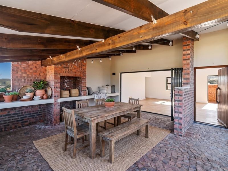 A spacious covered patio featuring exposed timber beams, a rustic brick fireplace, built-in concrete seating, and stone flooring, seamlessly connecting to the interior living space.