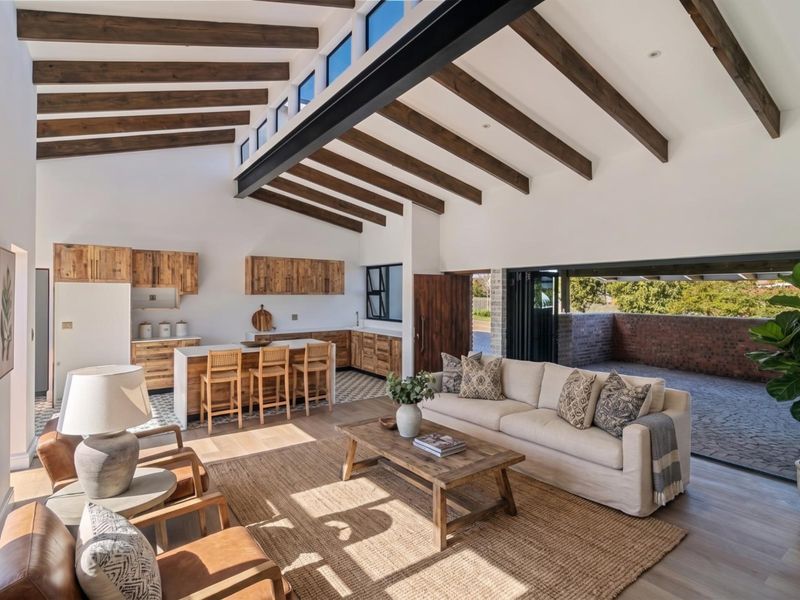 Spacious open-plan living and kitchen area featuring exposed timber beams, high ceilings with clerestory windows, and seamless indoor-outdoor flow through large stacking doors.