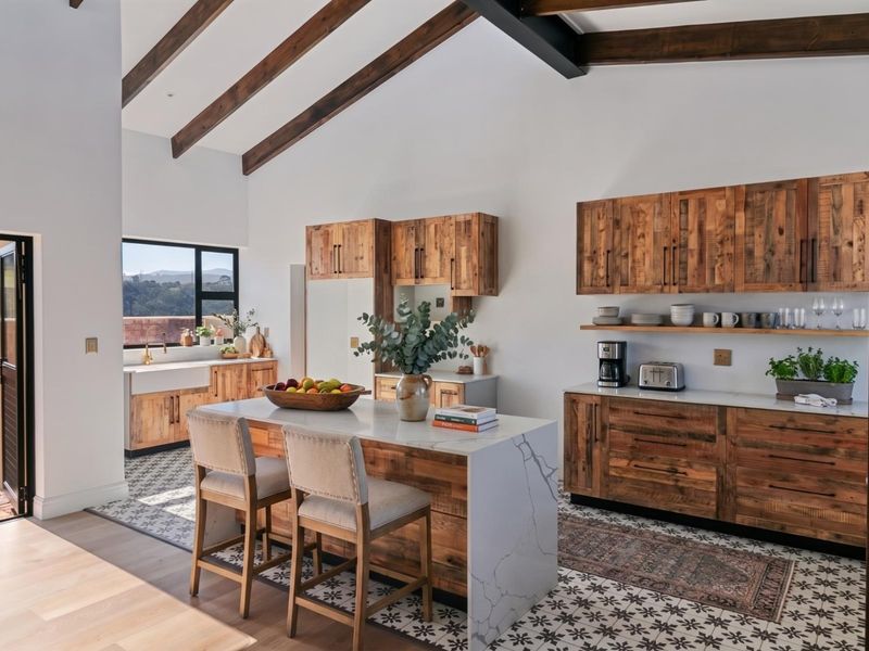 A beautifully designed kitchen featuring exposed timber beams, a marble waterfall island, custom wood cabinetry, and elegant patterned floor tiles with a vaulted ceiling.
