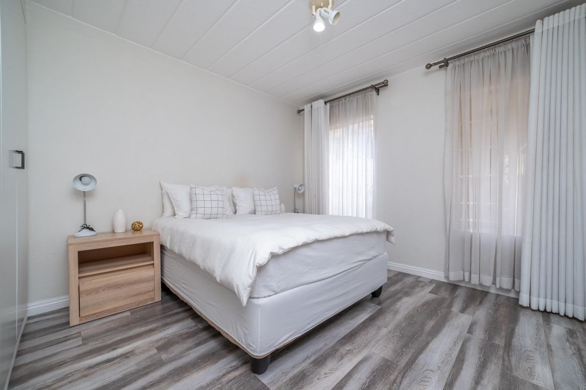 A bright and neutral bedroom featuring modern wood-look laminate flooring, built-in wardrobe, and dual window treatments for natural light control.