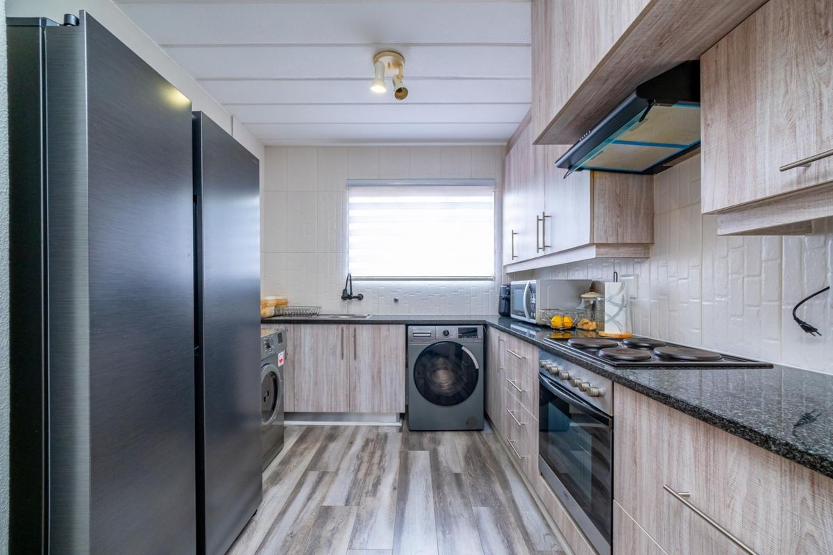 A functional kitchen featuring wood-look cabinetry, granite countertops, a built-in oven, hob, extractor fan, and integrated laundry appliance space.