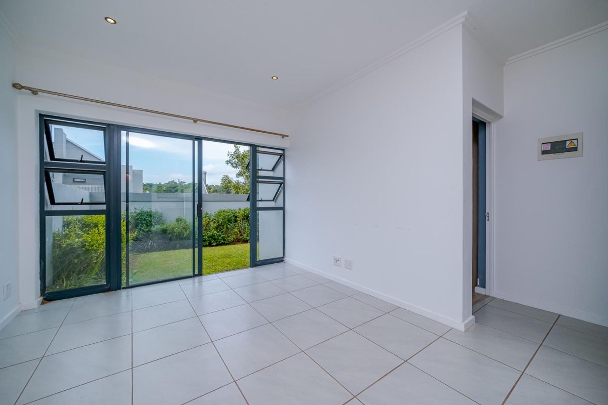 A bright, empty living area featuring large sliding glass doors that open onto a private garden, finished with neutral floor tiles and recessed lighting.