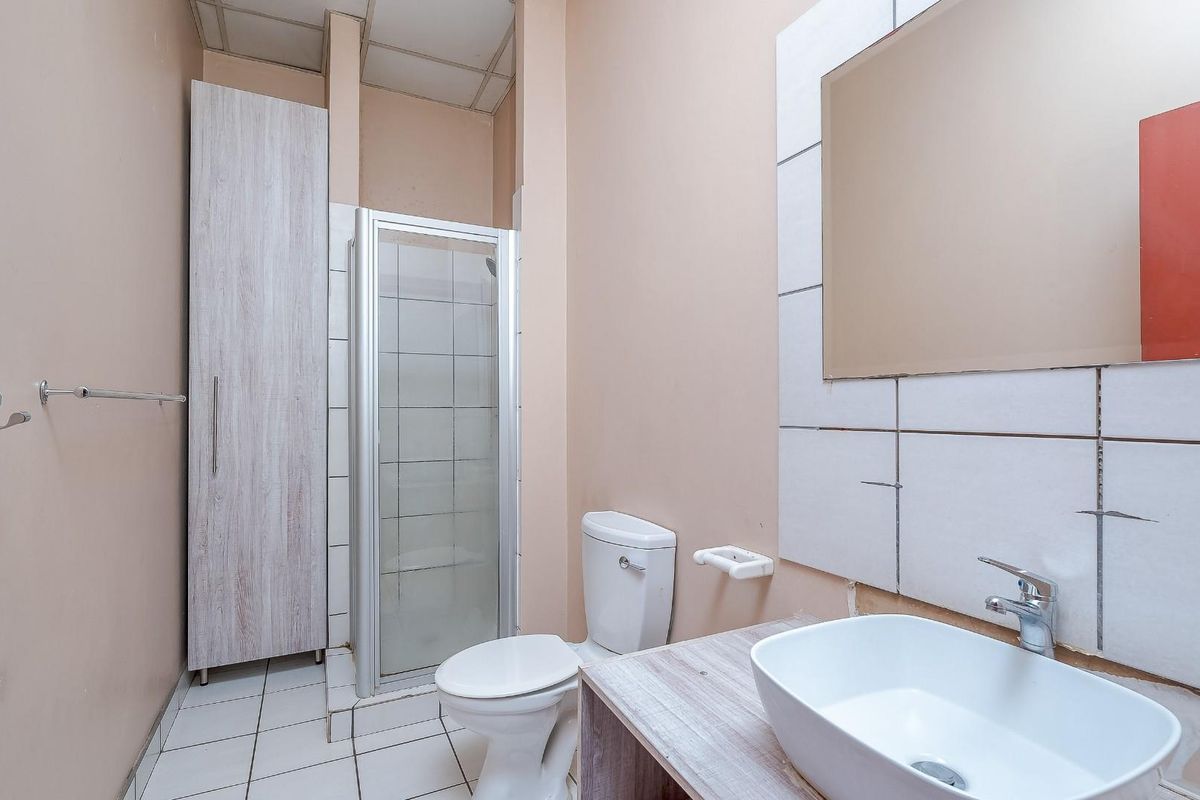 A compact bathroom featuring a shower cubicle, a white toilet, and a vessel sink vanity with unfinished wall tiling.