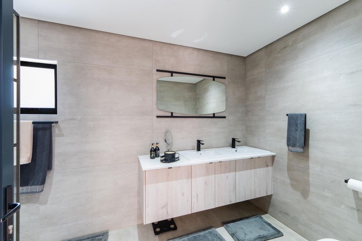 Modern bathroom featuring a sleek double vanity with integrated sinks, black fixtures, and large format neutral wall tiles.