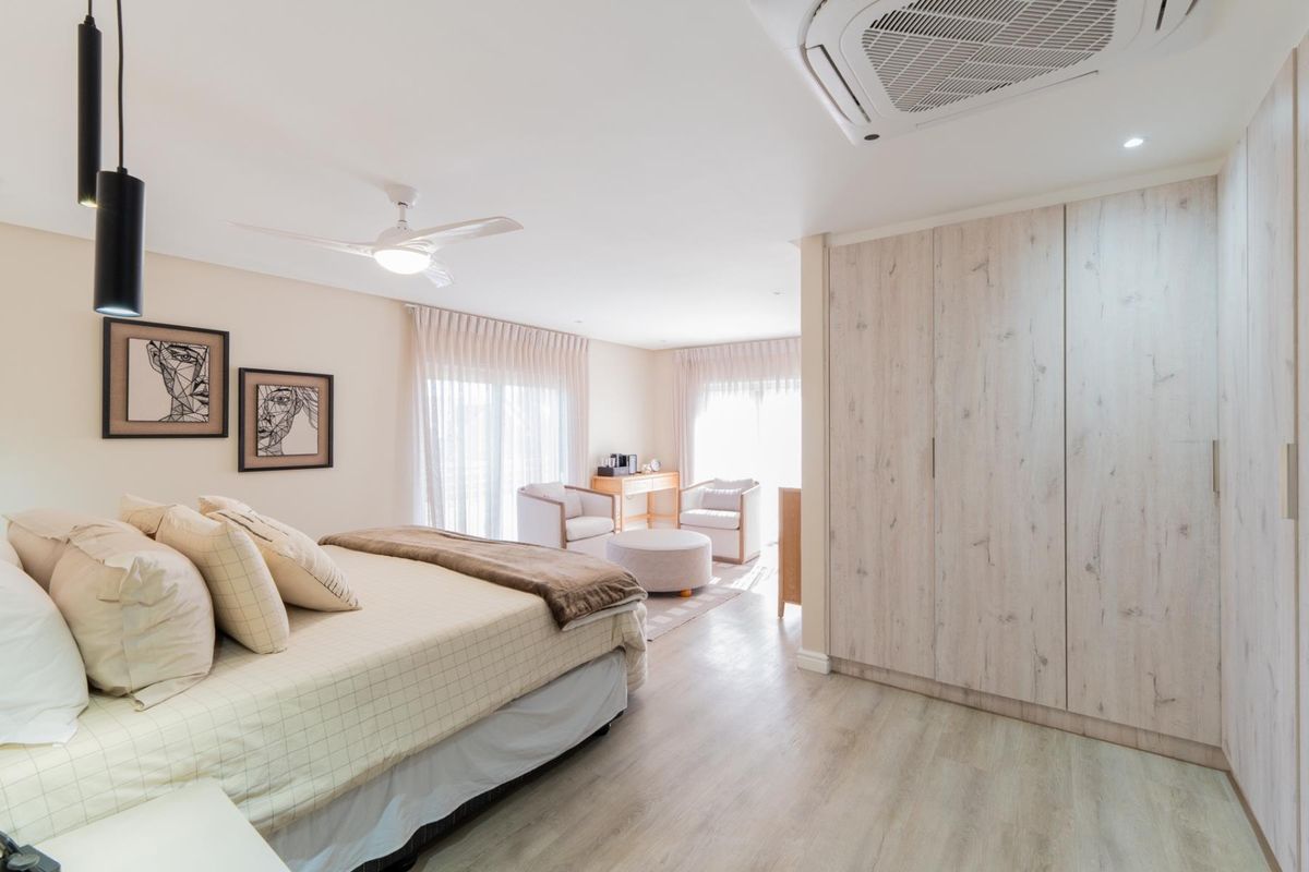 Spacious bedroom featuring light wood-look laminate flooring, extensive built-in cupboards, a ceiling fan, and integrated air conditioning, with direct access to a patio area.