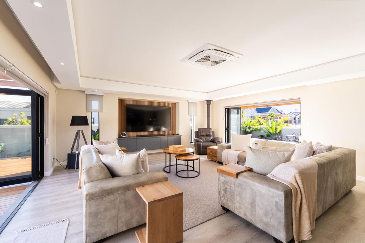 Spacious, modern living room featuring a slatted timber media wall, built-in cabinetry, ceiling-mounted air conditioning, and seamless access to the outdoor patio via bi-fold doors.