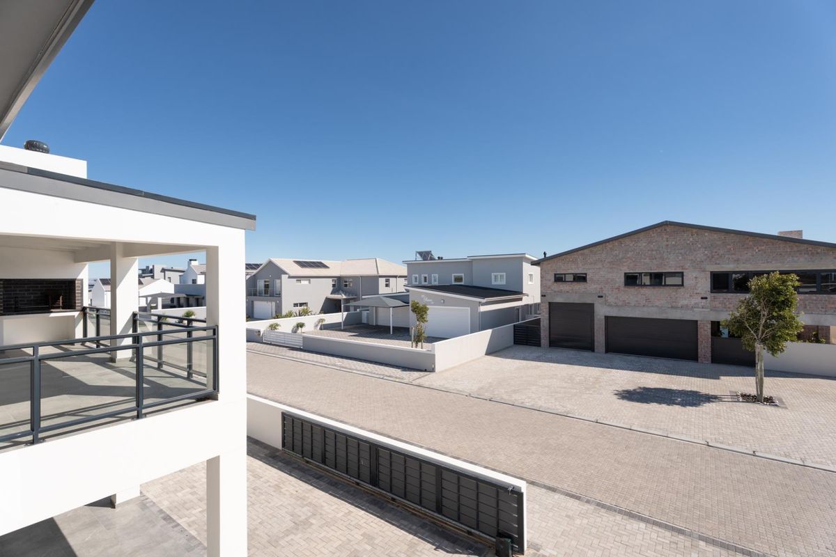 Elevated view overlooking a modern residential street with paved driveways, contemporary garage structures, and a balcony in the foreground.