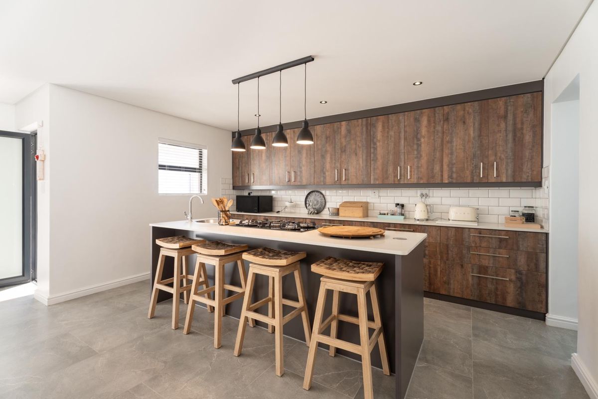 Modern kitchen featuring wood-grain cabinetry, a central island with a built-in gas hob, stone countertops, and subway tile backsplash.