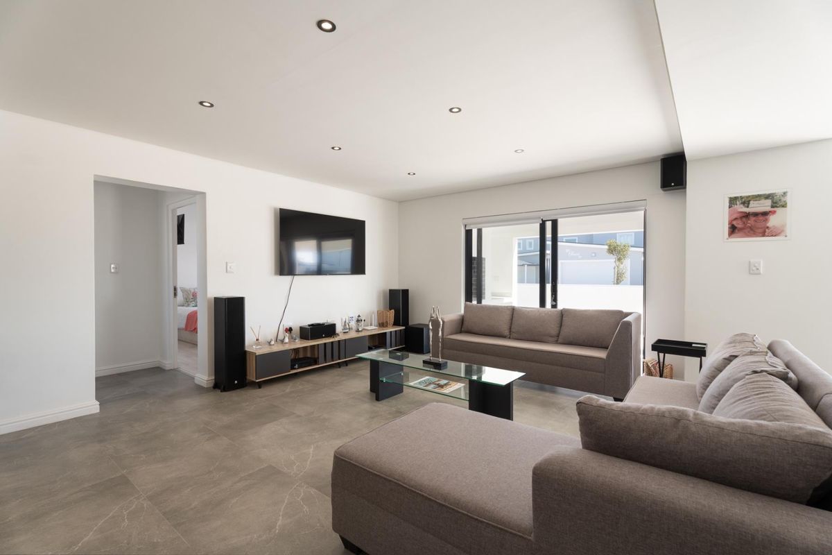 Modern living room featuring large format floor tiles, recessed downlighting, and sliding glass doors providing access to the outdoor area.