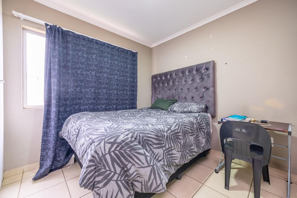 A functional bedroom featuring tiled flooring and a window with curtain track, providing a simple and practical living space.