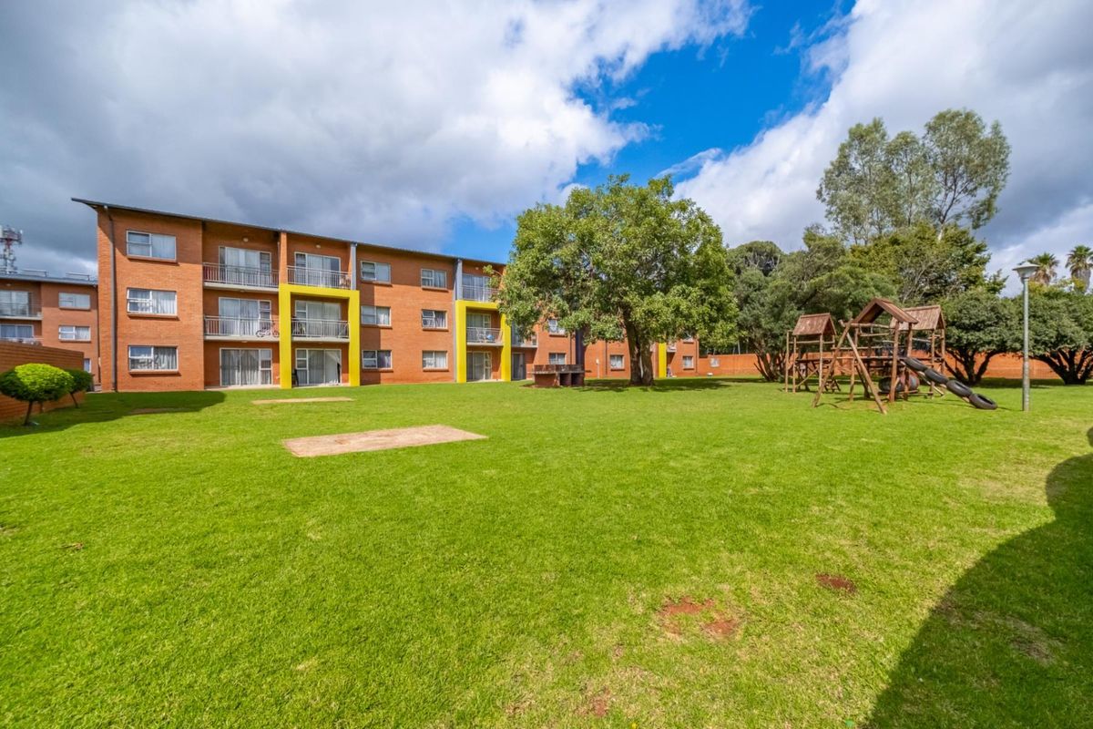 A view of the apartment complex exterior featuring a large communal lawn, mature trees, and a children's play area.