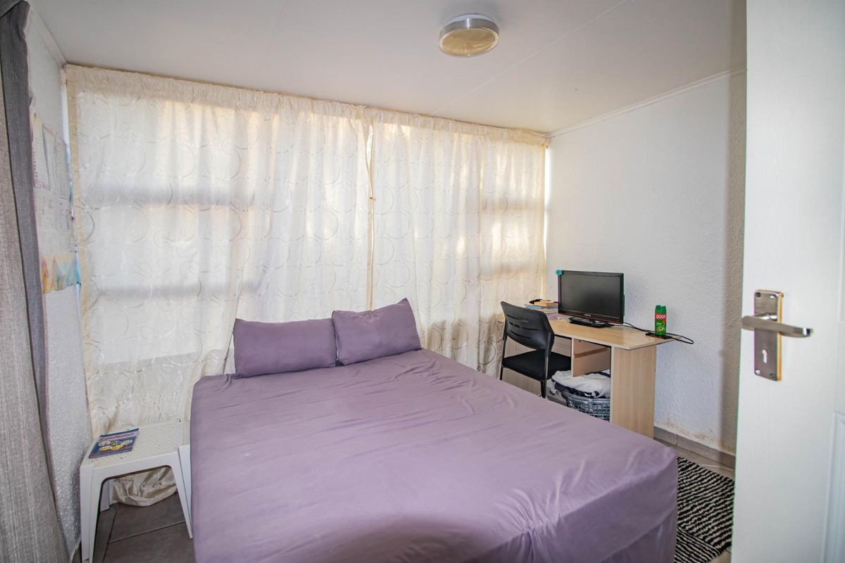 A functional bedroom featuring tiled flooring, a ceiling-mounted light fixture, and large windows covered by curtains.
