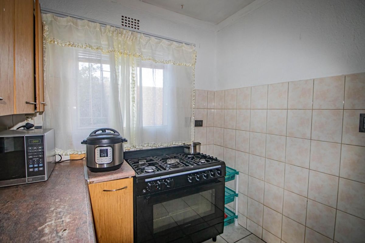 A compact kitchen featuring a gas stove, tiled splashback, and wooden cabinetry, offering a functional layout in need of cosmetic updates.