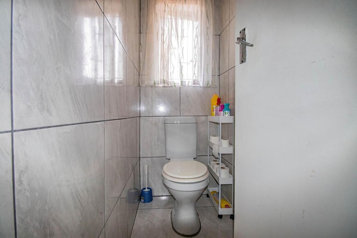 A compact guest bathroom featuring full-height wall tiling, a standard toilet, and a small window with privacy curtain.