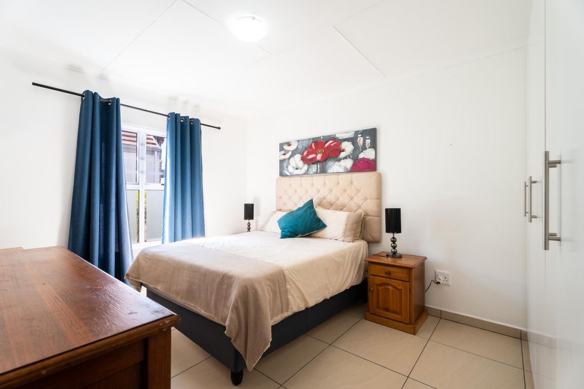 A well-maintained bedroom featuring neutral tiled flooring, a built-in wardrobe, and a window with curtain tracks.