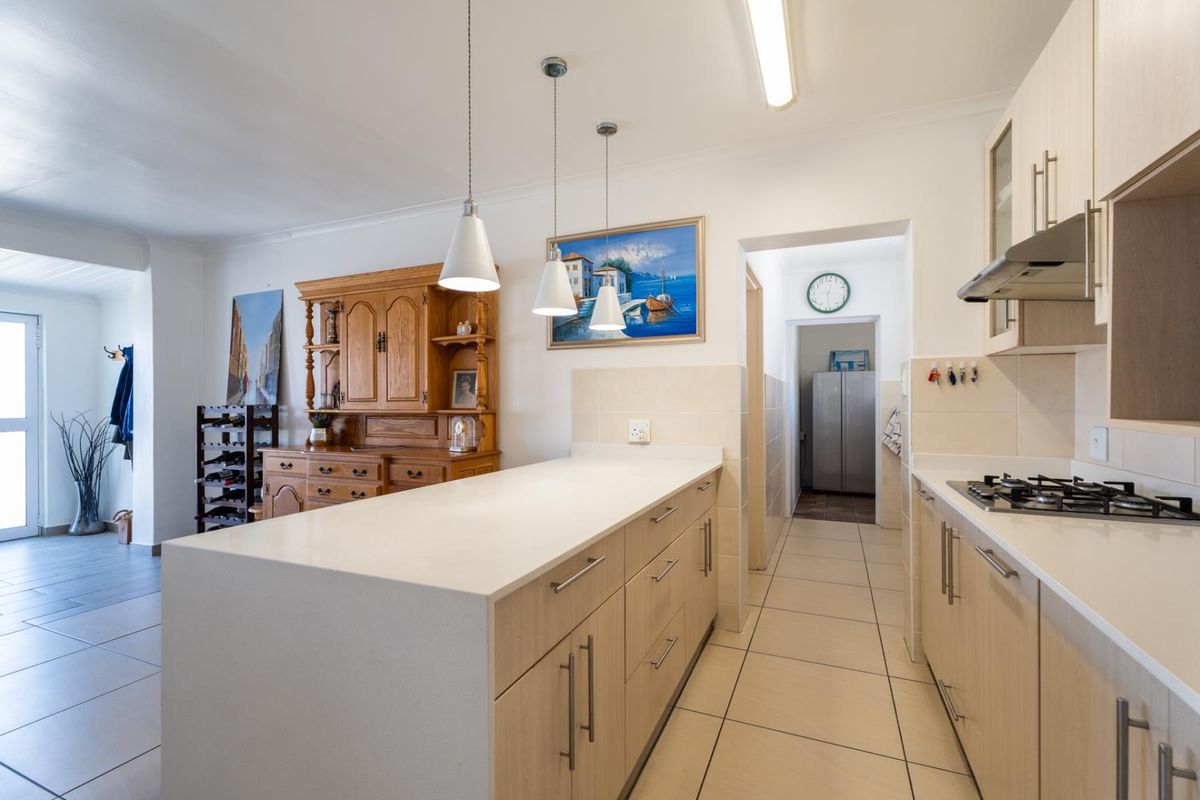 A functional kitchen featuring a central island, light wood cabinetry, gas hob with extractor, and tiled flooring, leading to a secondary utility area.
