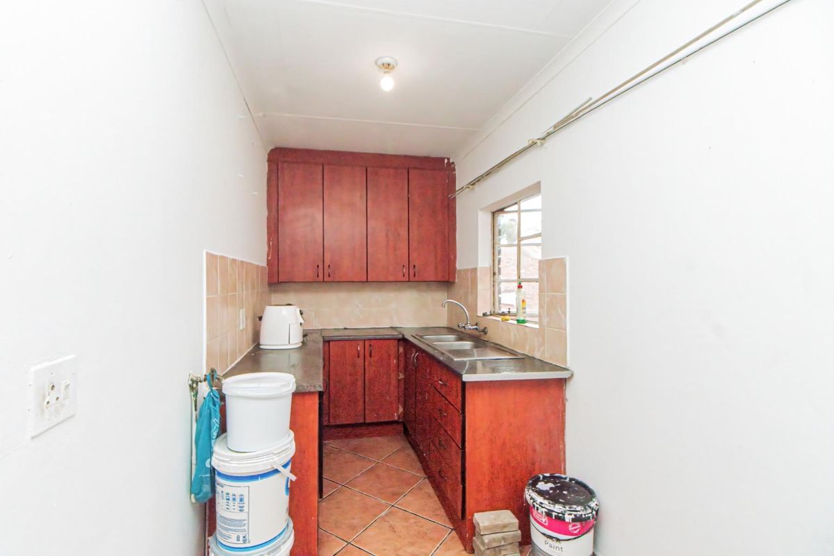 A compact kitchen featuring wooden cabinetry, a stainless steel double sink, and tiled flooring, offering a functional space in need of cosmetic updates.