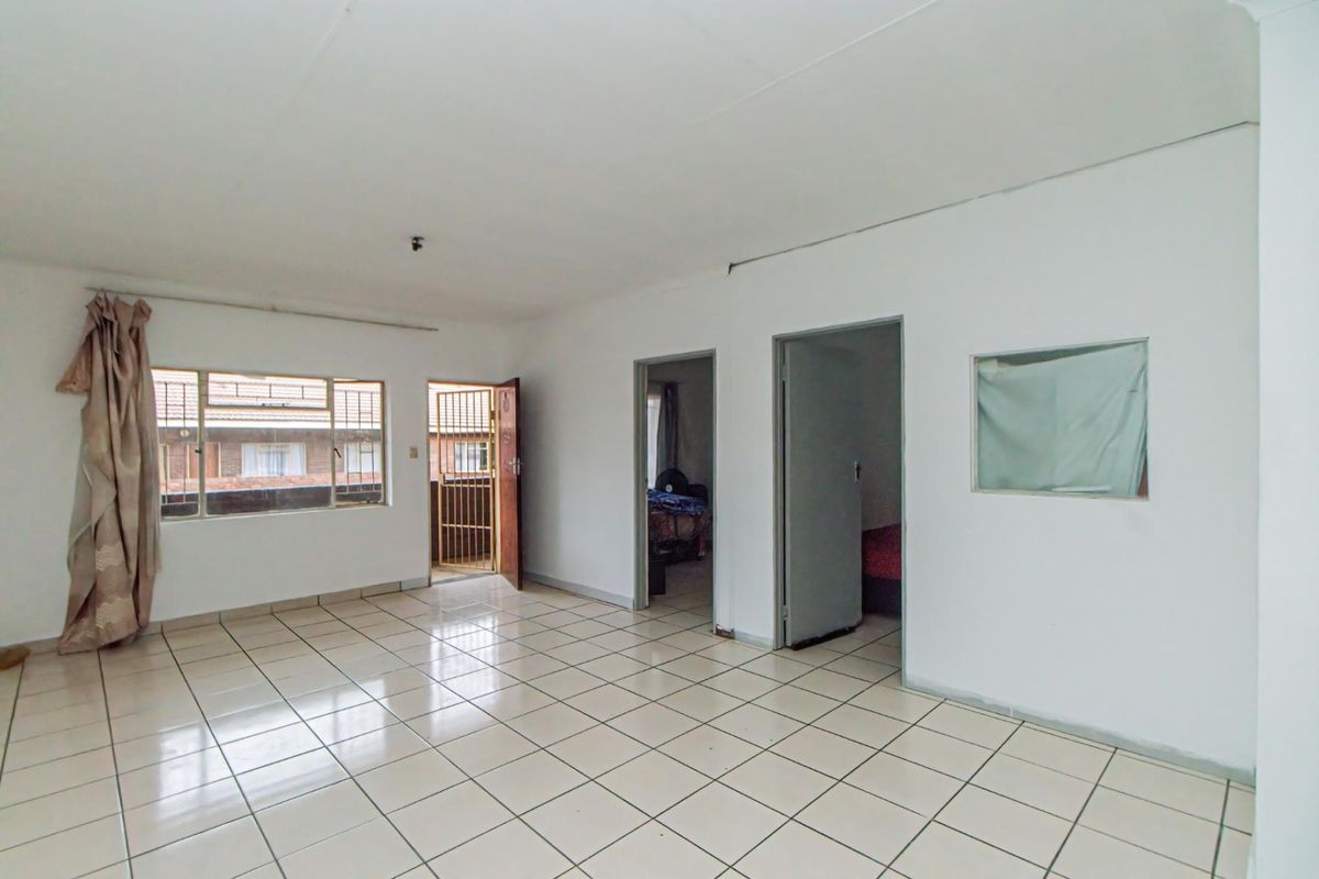 An empty living area featuring tiled flooring, multiple doorways leading to adjacent rooms, and a window providing natural light.