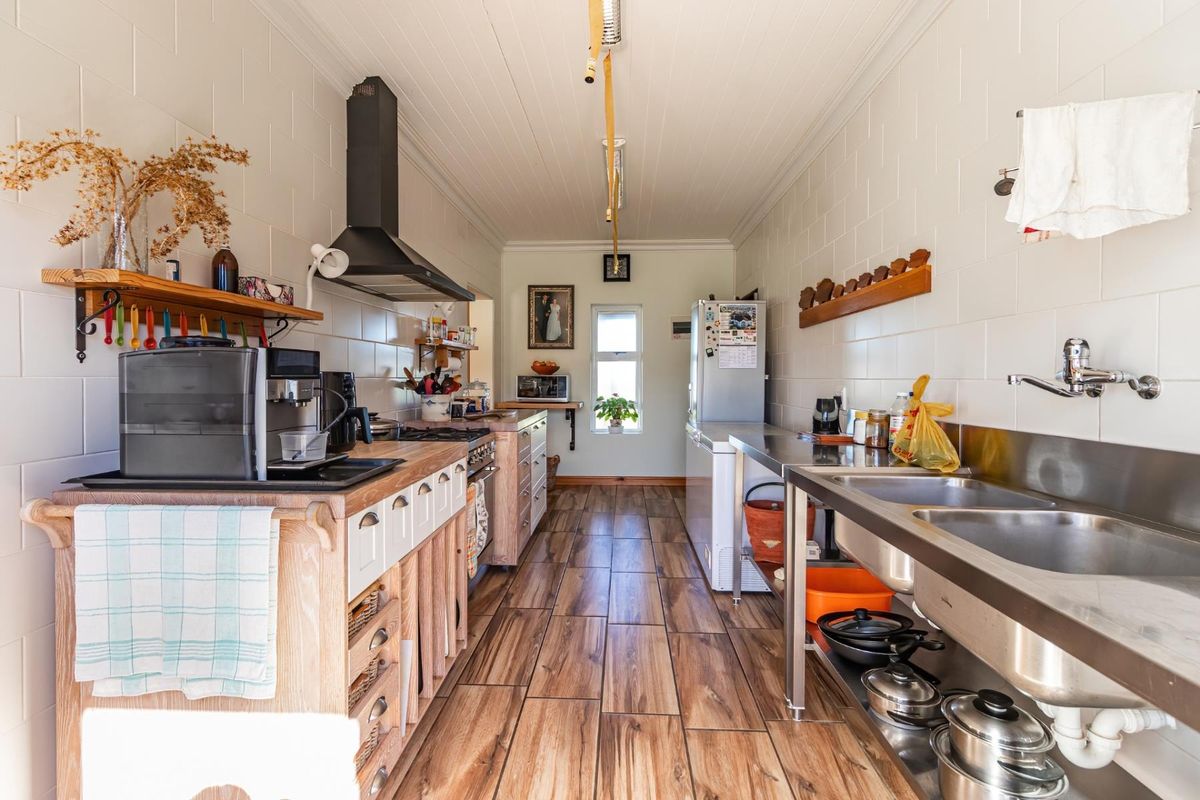 A functional farm-style kitchen featuring stainless steel double sinks, wooden cabinetry, a black extractor fan, and tiled wall finishes.