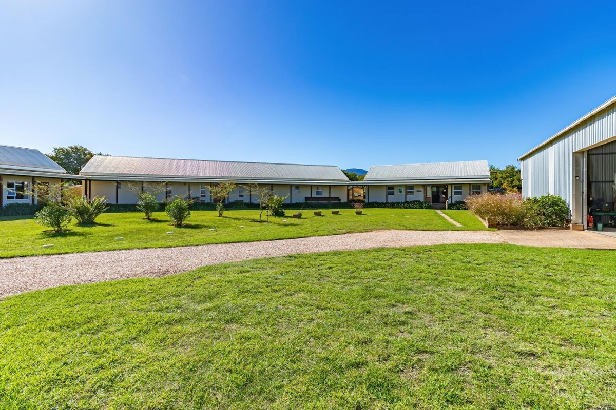 A wide view of the farm property featuring multiple outbuildings, a gravel driveway, and well-maintained lawn areas under a clear blue sky.