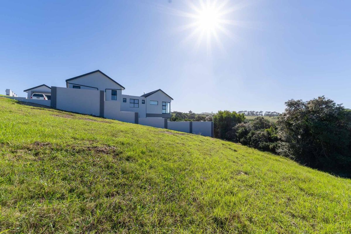 A view of a sloping residential plot featuring established green grass and a modern multi-level home in the background.