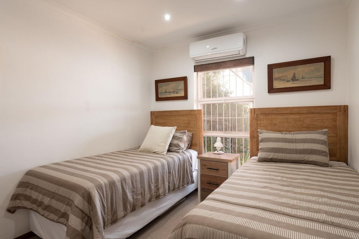 A well-maintained bedroom featuring a split-system air conditioning unit, security bars on the window, and neutral finishes.