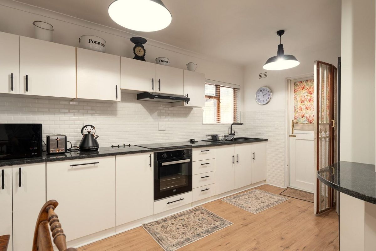 A well-maintained kitchen featuring white cabinetry, black granite countertops, a built-in oven, extractor fan, and subway tile backsplash with wood-look flooring.