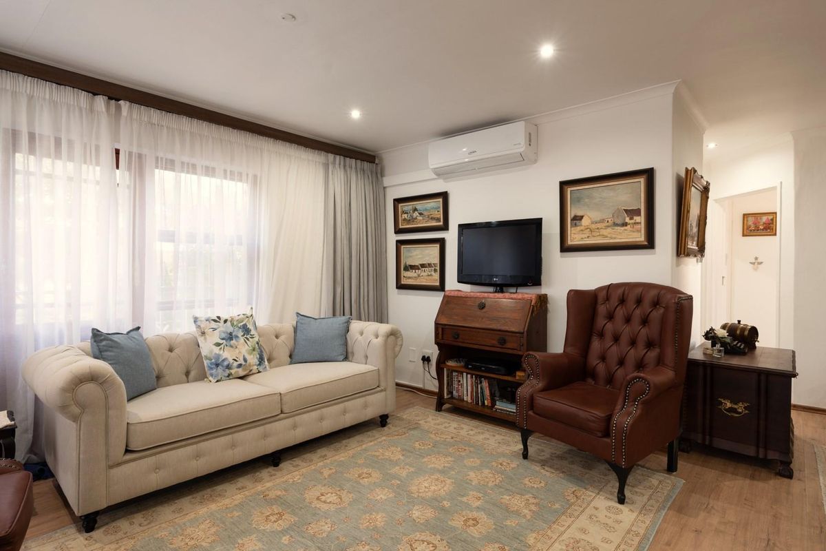 A comfortable living room featuring recessed downlighting, a wall-mounted air conditioning unit, and large windows with curtain tracks.