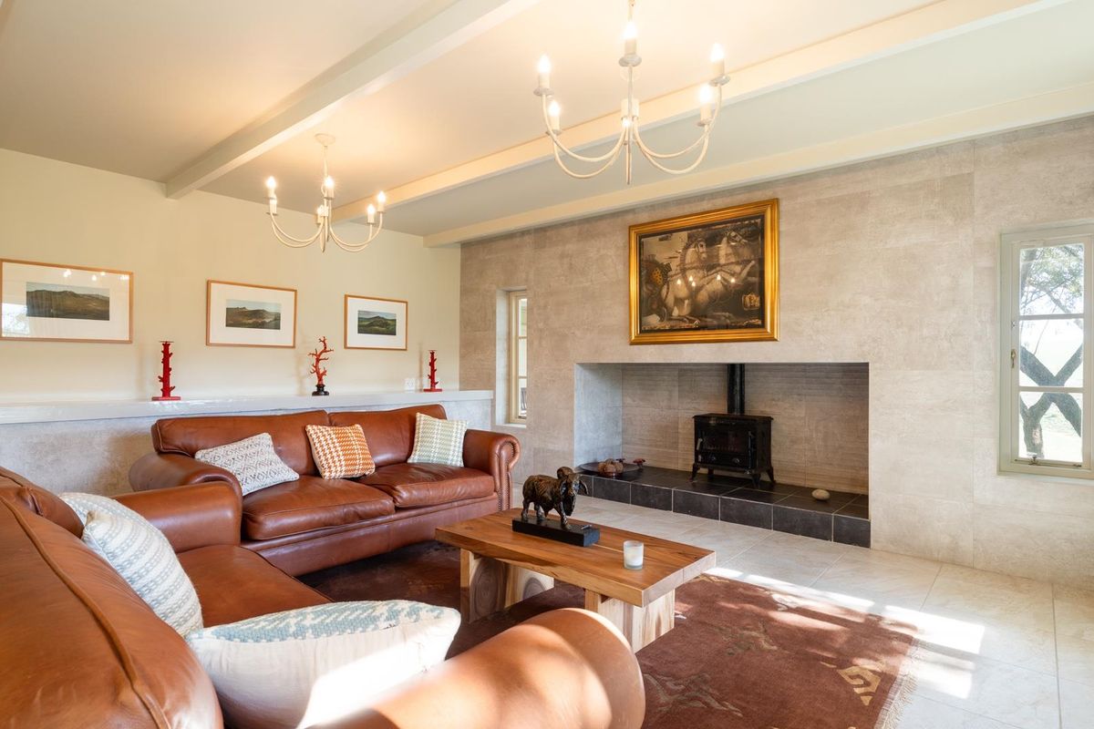 A spacious living room featuring a large stone-clad fireplace with a built-in wood-burning stove, exposed ceiling beams, and tiled flooring.