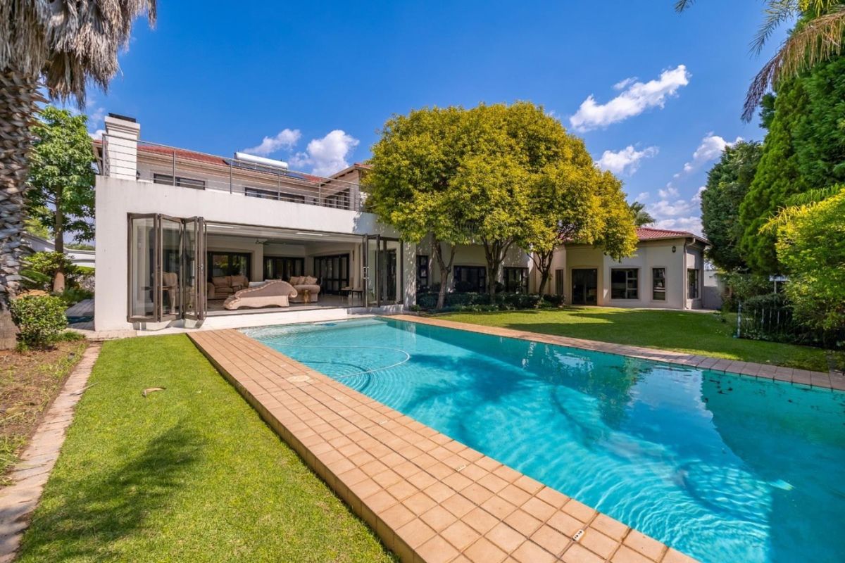 Spacious rear garden featuring a large swimming pool, manicured lawn, and seamless indoor-outdoor flow through expansive folding glass doors to the main residence.