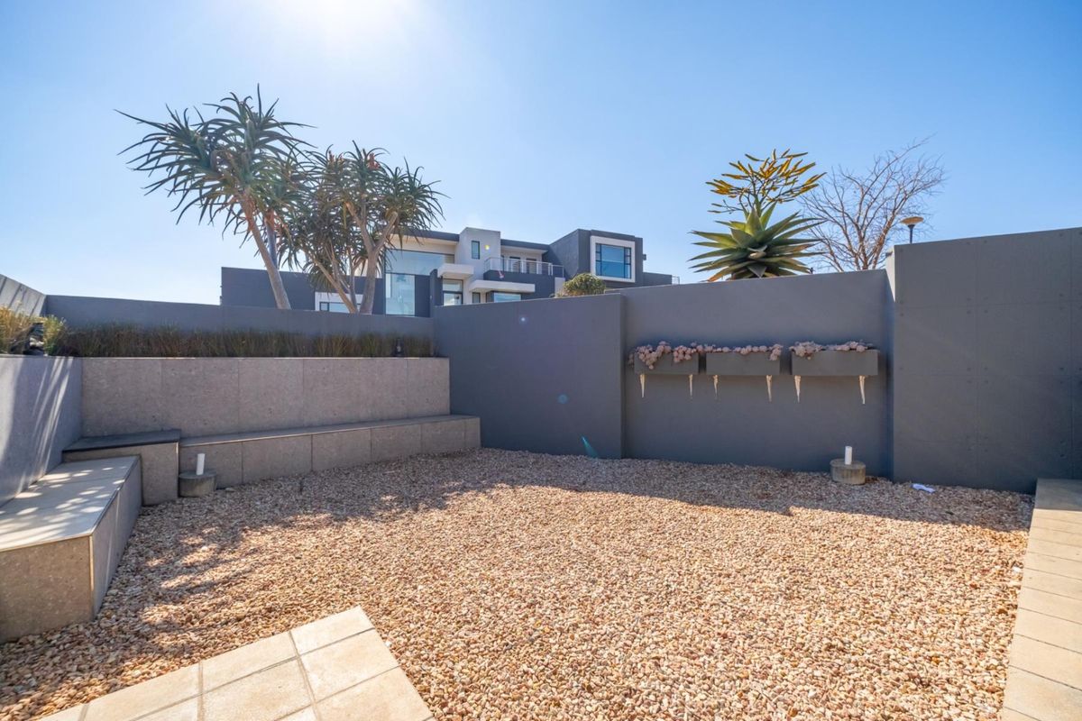 A modern rear courtyard featuring a built-in stone bench, gravel landscaping, and wall-mounted planters, set against a contemporary multi-story home.