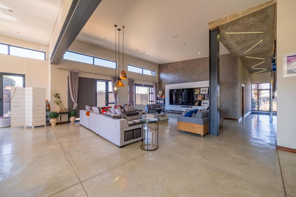 Spacious open-plan living area featuring polished concrete floors, high ceilings with exposed steel beams, and modern built-in media cabinetry.