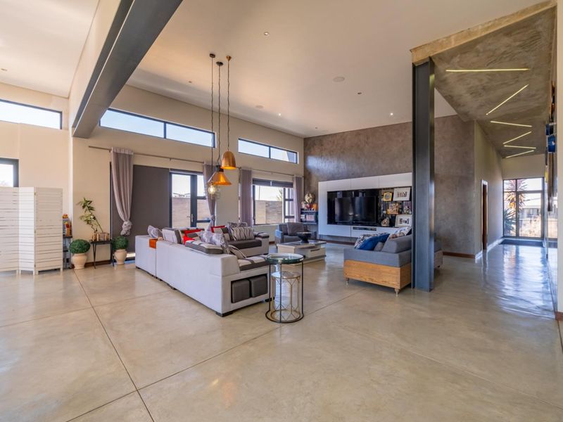 Spacious open-plan living area featuring polished concrete floors, high ceilings with exposed steel beams, and modern built-in media cabinetry.