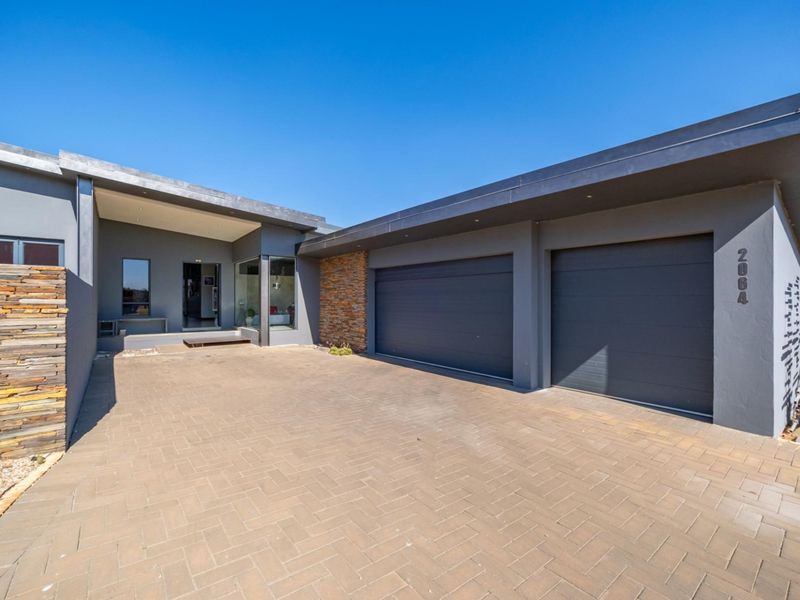 Modern front elevation featuring a double garage, paved driveway, and striking stone cladding accents, presenting a clean and contemporary architectural style.