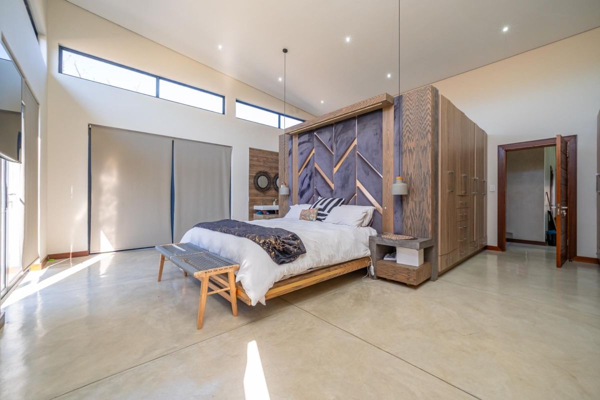 Spacious modern bedroom featuring polished concrete floors, high ceilings with clerestory windows, and a custom built-in wardrobe and headboard unit.