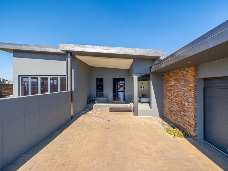 Modern front elevation featuring a paved driveway, stone cladding accent wall, covered entrance, and integrated garage.