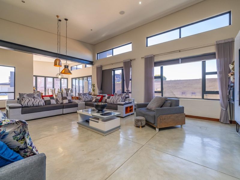 Spacious open-plan living area featuring polished concrete floors, high ceilings with clerestory windows, and modern architectural lighting, creating a bright and airy atmosphere.