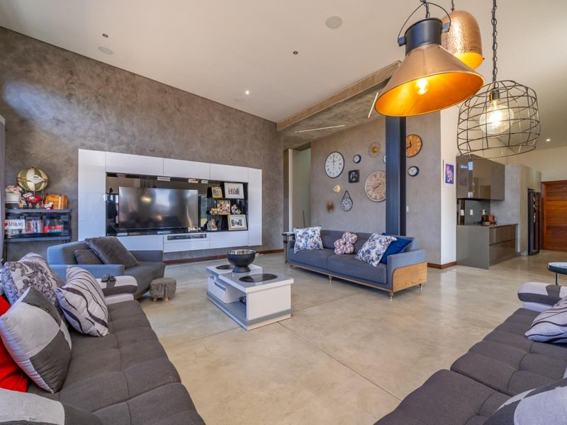 Spacious open-plan living area featuring polished concrete floors, a modern built-in media unit, and high ceilings with contemporary industrial-style pendant lighting.