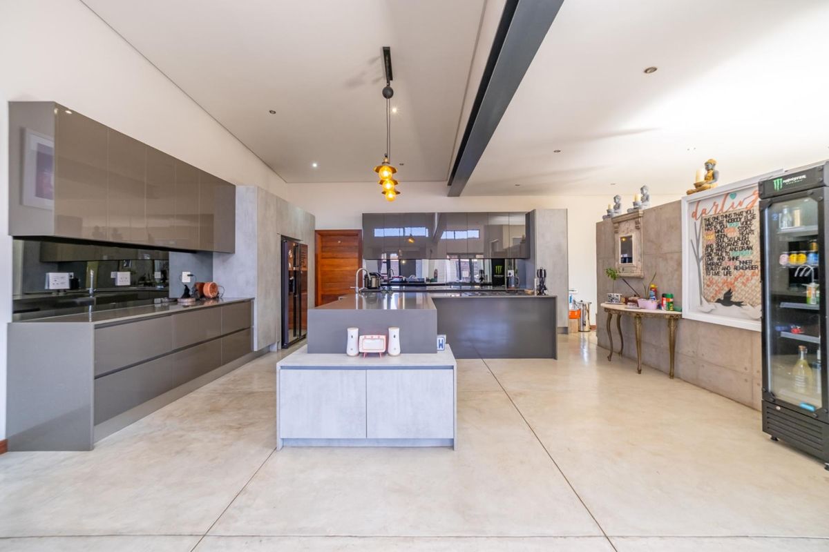 Modern open-plan kitchen featuring sleek high-gloss cabinetry, a central island, polished concrete floors, and contemporary lighting fixtures.