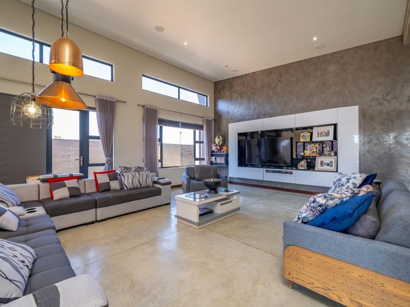 Spacious modern living room featuring polished concrete floors, a large built-in media wall, and high ceilings with clerestory windows for abundant natural light.