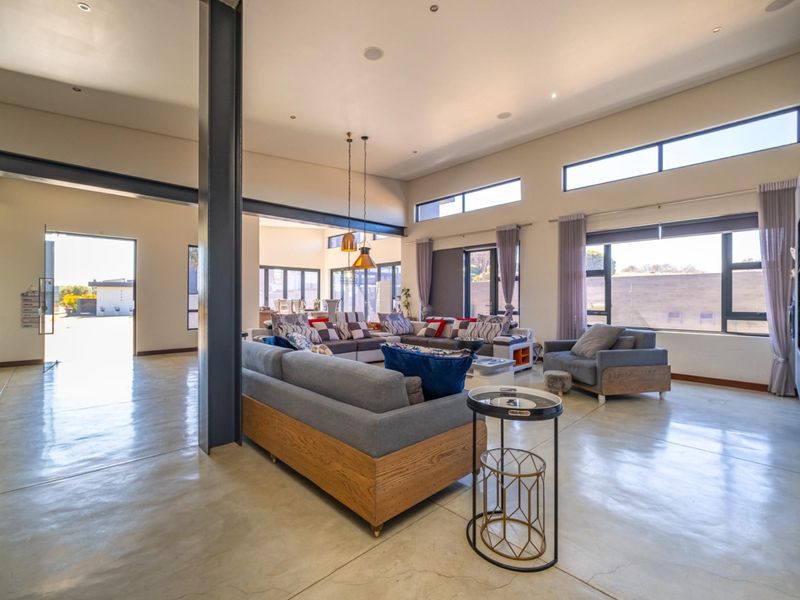 Spacious open-plan living area featuring polished concrete floors, high ceilings with exposed steel structural elements, and abundant natural light through large windows.